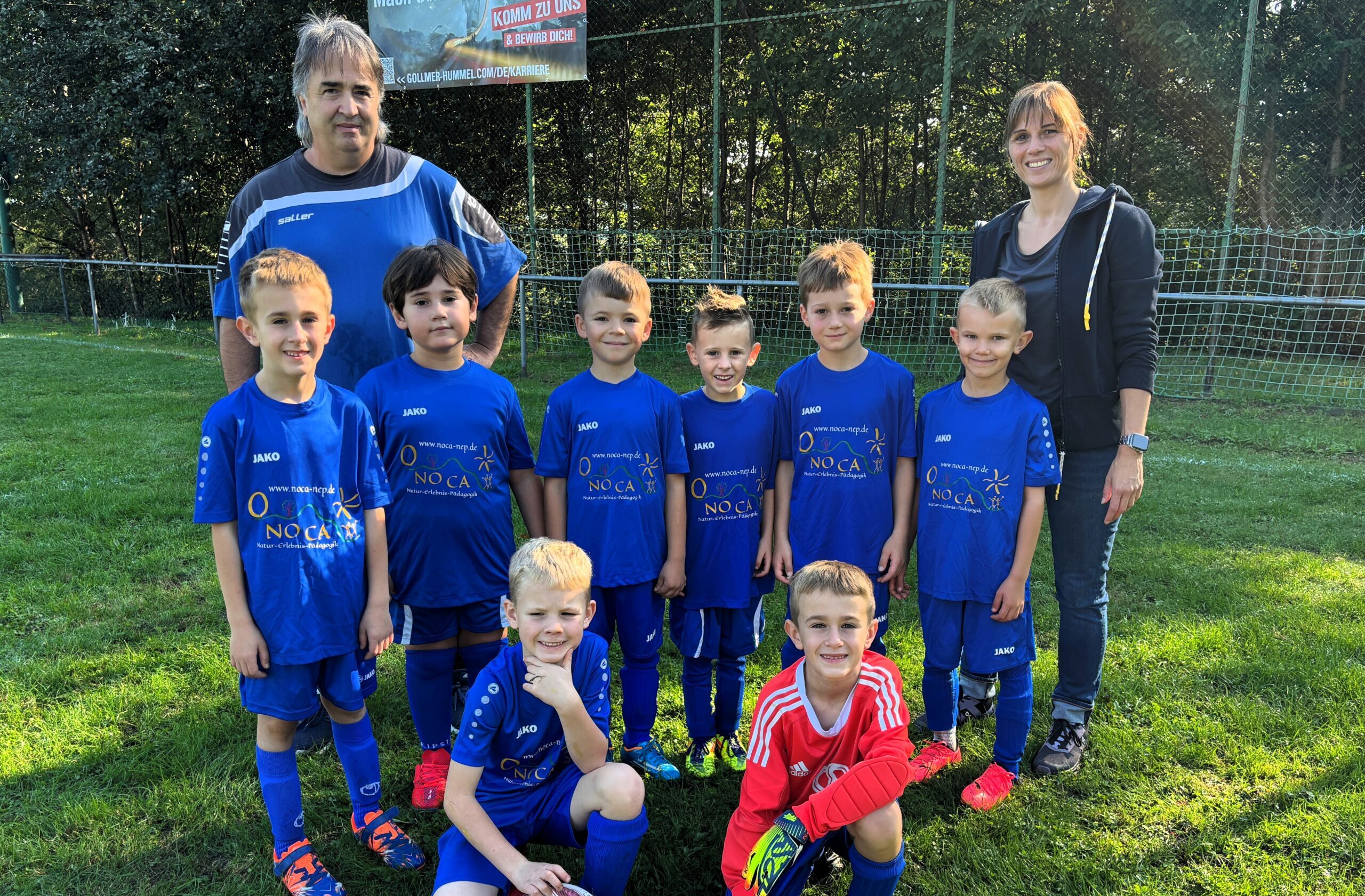 Gruppenbild einer Jugend Fußbalmannschaft mit Torwart in blauen Trikots und zwei erwachsenen Personen