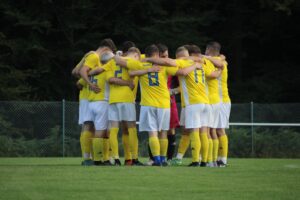 Mannschaftsfoto der Sportfreunde Dobel umarmend auf dem Spielfeld in gelben Trikots