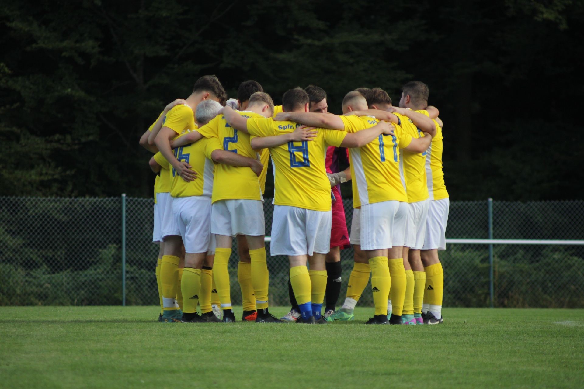 Mannschaftsfoto der Sportfreunde Dobel umarmend auf dem Spielfeld in gelben Trikots