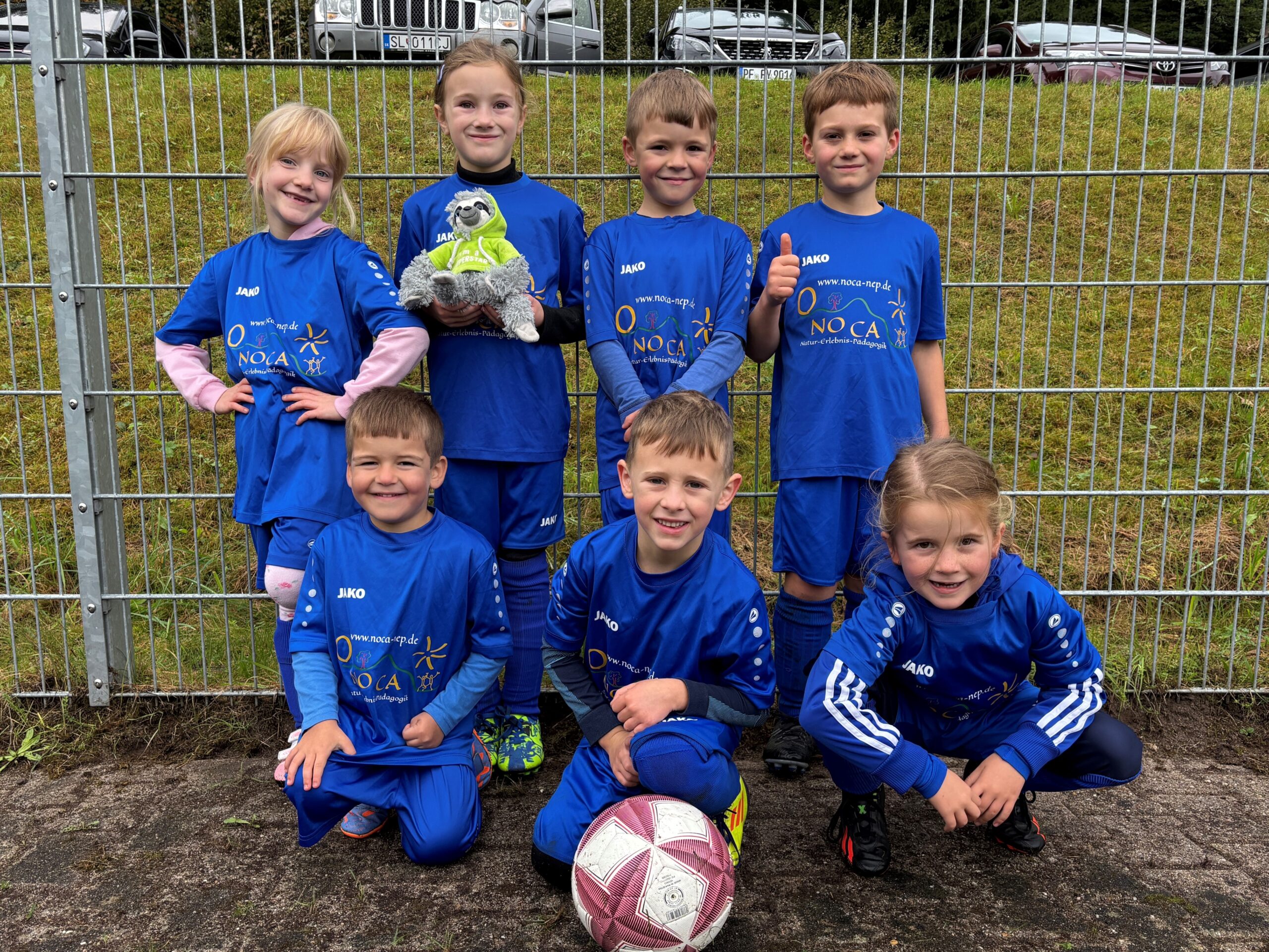 Gruppenbild mehrerer jugendlicher Fußbalspieler in blauen Trikots und einem Fußball