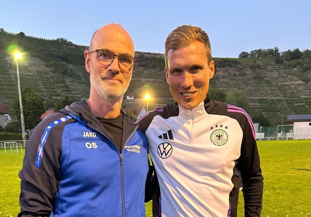 Zweier Gruppenbild lächelnd mit Spielfeld im Hintergrund bei Flutlicht