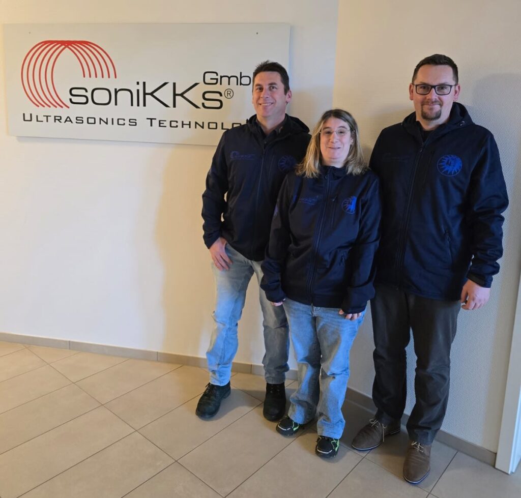 Gruppenbild: 3 Personen stehen von einem Logo mit der Aufschrift Sonikks GmbH