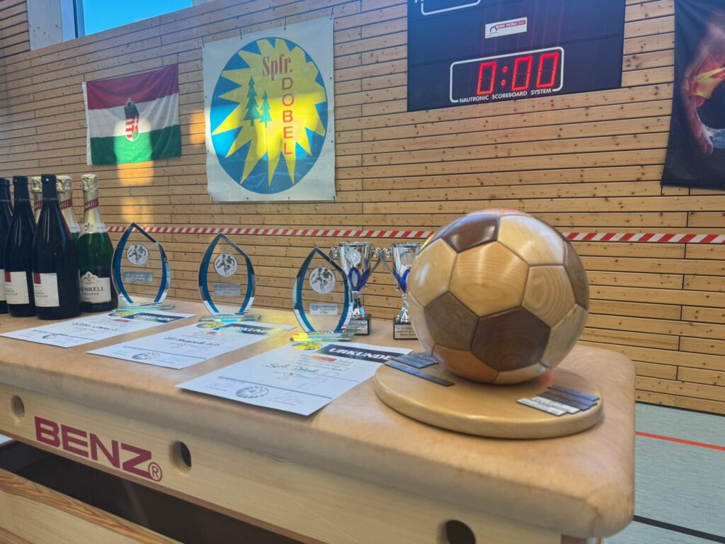 Drei Pokale und Sektflaschen auf einem Tisch in einer Turnhalle stehend