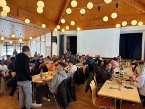 Raum mit Tischen und Sitzmöglichkeiten voller Vereinsmitglieder essend und sprechend