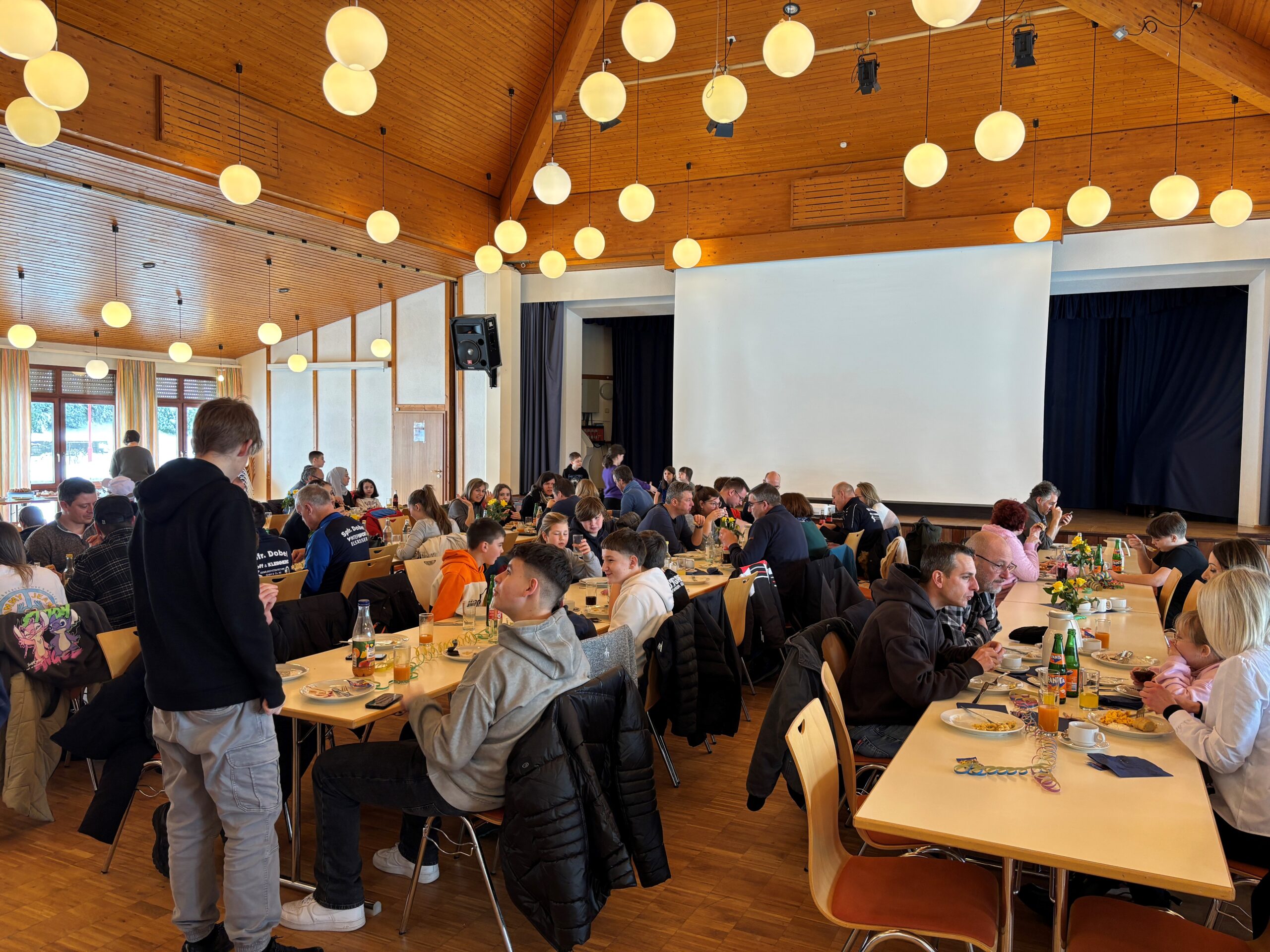 Raum mit Tischen und Sitzmöglichkeiten voller Vereinsmitglieder essend und sprechend